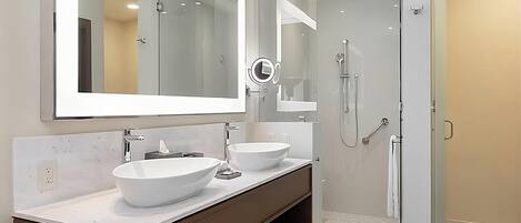 A modern bathroom with a large mirror, two sinks, a shower, and a towel rack.