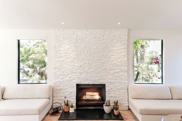 A living room with a stone fireplace, two sofas, and large windows with a view of greenery.