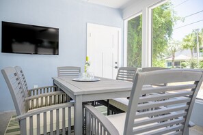 Un coin repas avec une table et des chaises, une bouteille de vin et un téléviseur fixé au mur.