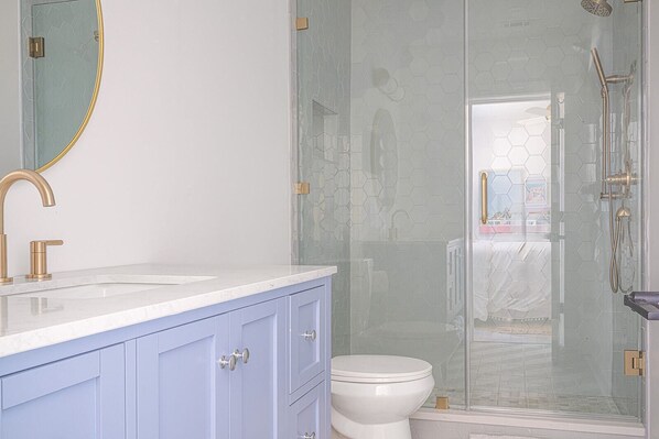 Un baño moderno con cabina de ducha de vidrio, inodoro blanco y tocador con grifo dorado.