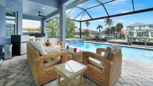 Zona de piscina con mobiliario de mimbre, una mesa de vidrio y vistas a la piscina y casas vecinas.