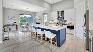 Una cocina moderna con una isla central, armarios blancos y un refrigerador de acero inoxidable.