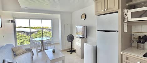 Un espace de vie compact comprenant un coin cuisine, un espace repas avec une table et des chaises, un canapé, un téléviseur, un ventilateur et un réfrigérateur.