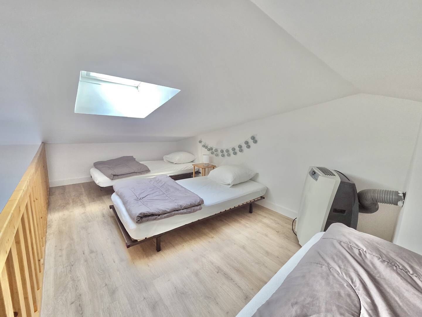 A small, modern room with a sloped ceiling, a skylight, a bed with a wooden frame, a bedside table, and a radiator.