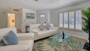 A living room with a white sofa, a glass coffee table, and a ceiling fan. - VILLA BEACH PARADISE – HEATED POOL & SPA | WATER VIEW (Bonita Springs)