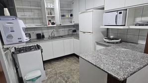 Una cocina compacta con armarios blancos, encimera de granito, microondas integrado y estufa a gas.
