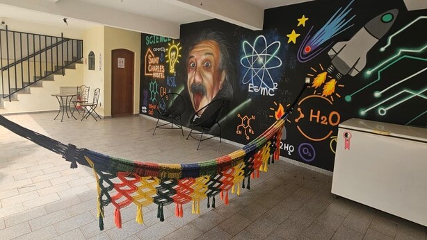 Amplia habitación con una hamaca, una escalera y un mural temático de ciencia en la pared.