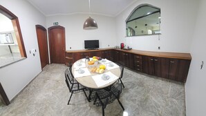 Un comedor con una mesa redonda, sillas y varios alimentos. Hay un televisor en la pared y un espejo sobre el mostrador.