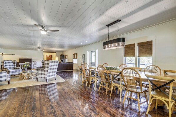 A spacious living room with a wooden floor, a dining area with a table and chairs, and a ceiling fan.