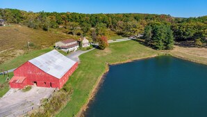 Ein rotes Bauernhaus mit weißem Dach, ein kleines weißes Gebäude und ein Teich.