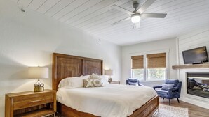 Ein Schlafzimmer mit einem hölzernen Bett, Nachttischen, einem blauen Sessel, einem Kamin und einem Deckenventilator.
