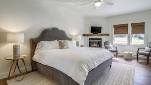 Ein Schlafzimmer mit einem großen Bett, zwei Nachttischen, einem Deckenventilator, einem Fernseher und einem Kamin.