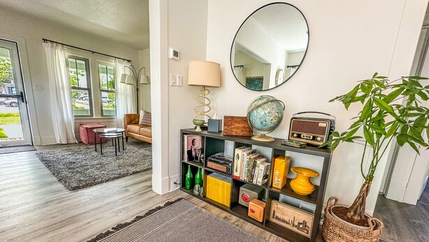 A living room with a sofa, a coffee table, a bookshelf with various items, a potted plant, and a large mirror on the wall.