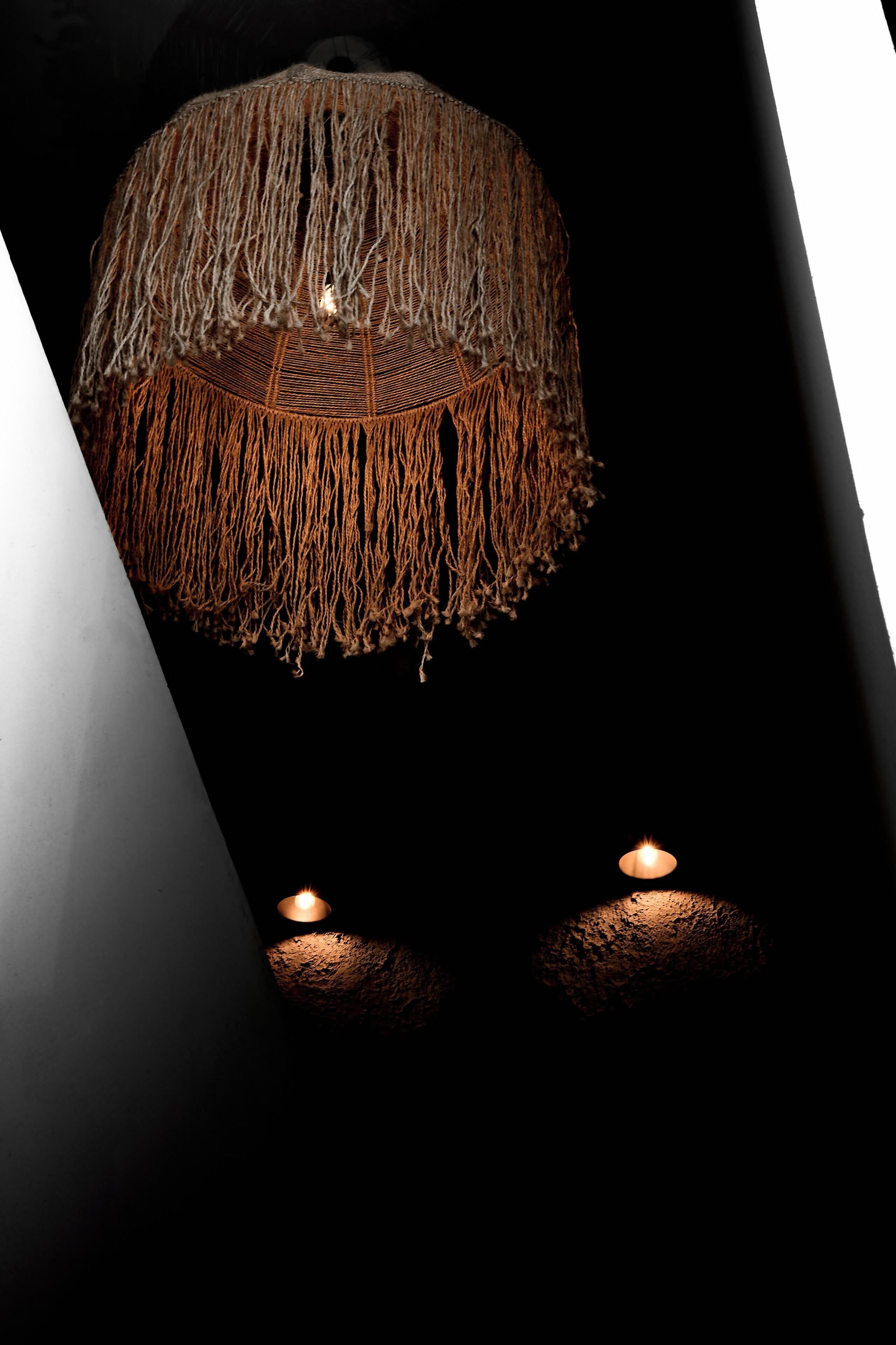 A hanging light fixture with a woven design and two candles on the floor.