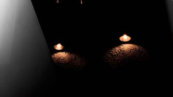 A hanging light fixture with a woven design and two candles on the floor.