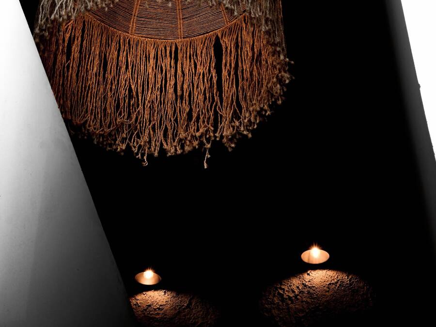A hanging light fixture with a woven design and two candles on the floor.