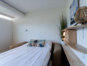 Une chambre à coucher comprenant un lit, une chaise, une table de chevet, une étagère fixée au mur, une plante en pot et un tableau.