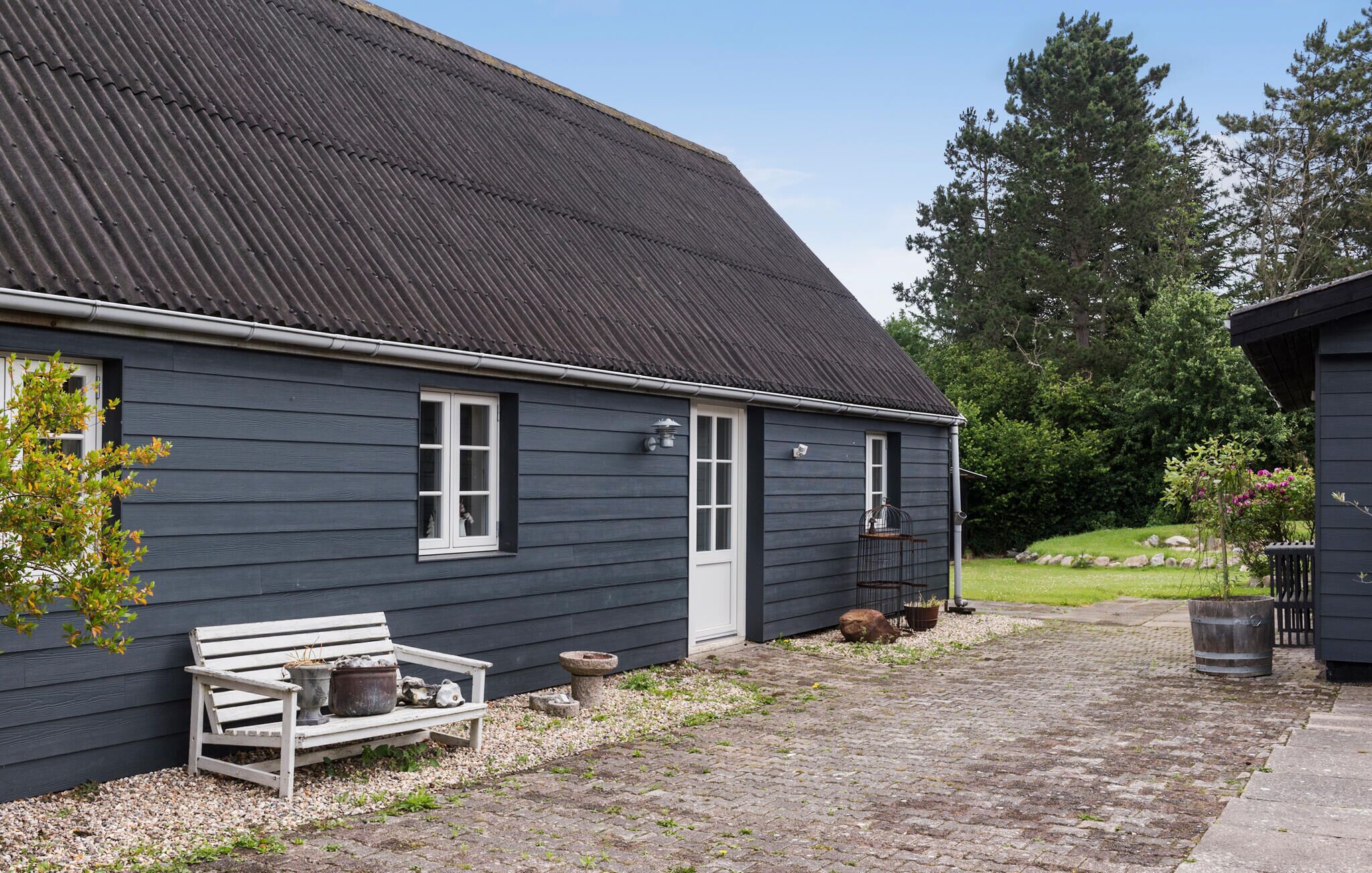 A dark wooden house with a sloped roof, a bench, and potted plants.