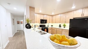 A modern kitchen with white countertops, wooden cabinets, a black refrigerator, and a bowl of lemons on the counter. - Charming 3BR with WiFi, AC and Parking in Marvelous Los Angeles (Los Angeles)