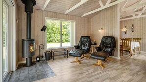 A cozy room with a wood-burning stove, two leather chairs, a dining table, and a view of greenery outside. - Pet friendly home in Tarm with WiFi (Tarm)