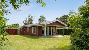 A red single-story house with a covered porch, a fenced yard, and a small shed. - Pet friendly home in Tarm with WiFi (Tarm)