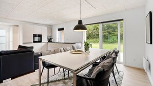 Une cuisine moderne avec des meubles blancs, un coin repas comprenant une table et des chaises, et une grande fenêtre donnant sur un paysage verdoyant.