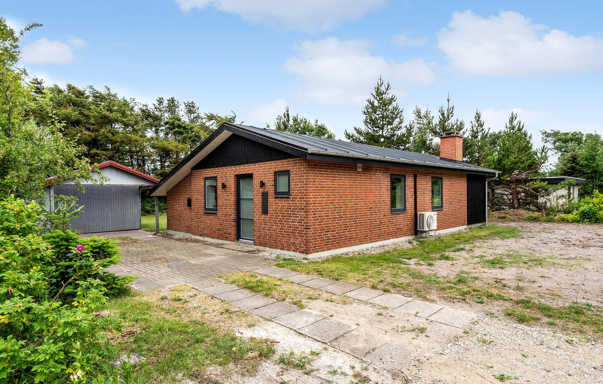 A small brick house with a sloped roof, a chimney, and a paved driveway.