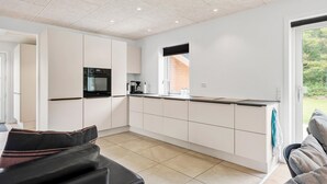 Une cuisine moderne avec des meubles blancs, un four encastré et une fenêtre donnant sur un espace verdoyant.