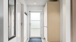 Un couloir avec une porte blanche, un miroir noir et blanc et un paillasson bleu.