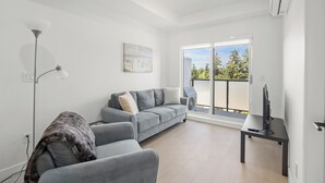 A modern living room with a grey sofa, a floor lamp, and a flat-screen TV on a black stand.