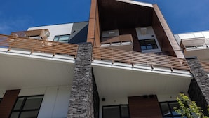 A modern multi-story building with a prominent stone facade, wooden balconies, and large windows.