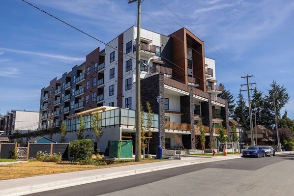 A multi-story residential building with balconies, a parking area, and a street view.
