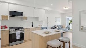 A modern kitchen with white cabinetry, a central island, and a dining area with two stools.