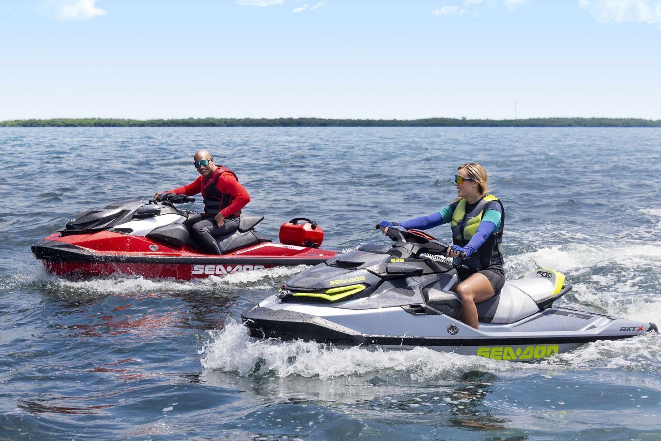 Dos personas sobre motos acuáticas en un cuerpo de agua, con una costa distante.