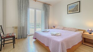 A bedroom with a bed, a chair, a nightstand, a lamp, and a painting on the wall.