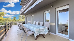 A balcony with a table and chairs, a railing, and a view of the sky and trees.