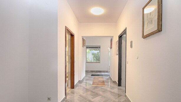 A hallway with a herringbone floor pattern, white walls, and a ceiling light.