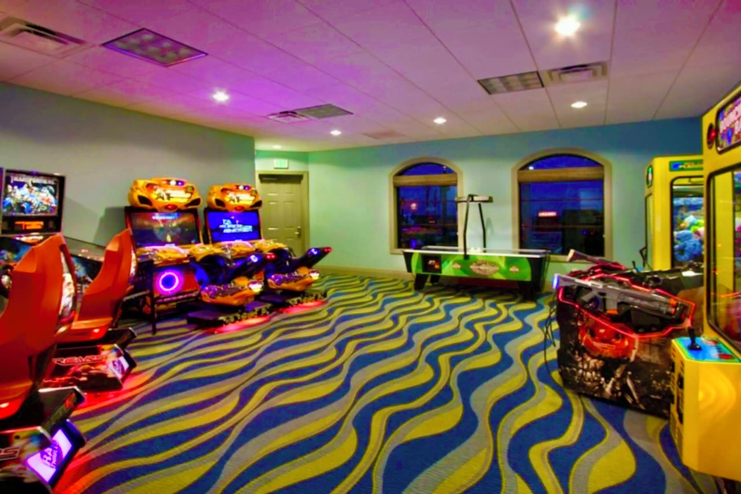 A gaming area with arcade machines, a pool table, and a large carpet with a wavy pattern.