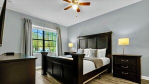 A bedroom with a large bed, a desk, a nightstand, and a ceiling fan.