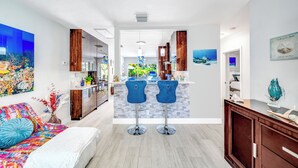 Een moderne keuken met houten kasten, een centraal eiland met barkrukken en een kleurrijke muurschildering aan de linker muur.