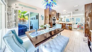 Een moderne keuken met een centraal eiland, een eetgedeelte met een blauwe beklede stoel en een grote decoratieve kroonluchter.