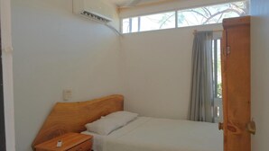 A small, single-bed room with a wooden headboard, a bedside table with a lamp, and a window with curtains. - Casa Firefly (Puerto Escondido)