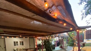 An outdoor patio area with wooden tables and benches, a covered seating area, and string lights. - Casa Firefly (Puerto Escondido)
