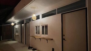 A dimly lit hallway with a wooden bench, a door, and a hanging light fixture. - Casa Firefly (Puerto Escondido)