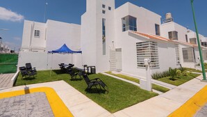 A modern building with white exterior walls, a flat roof, and a small garden area with grass and outdoor seating. - FFamily House & Water Park Tlayecac 3 BR (Ayala)