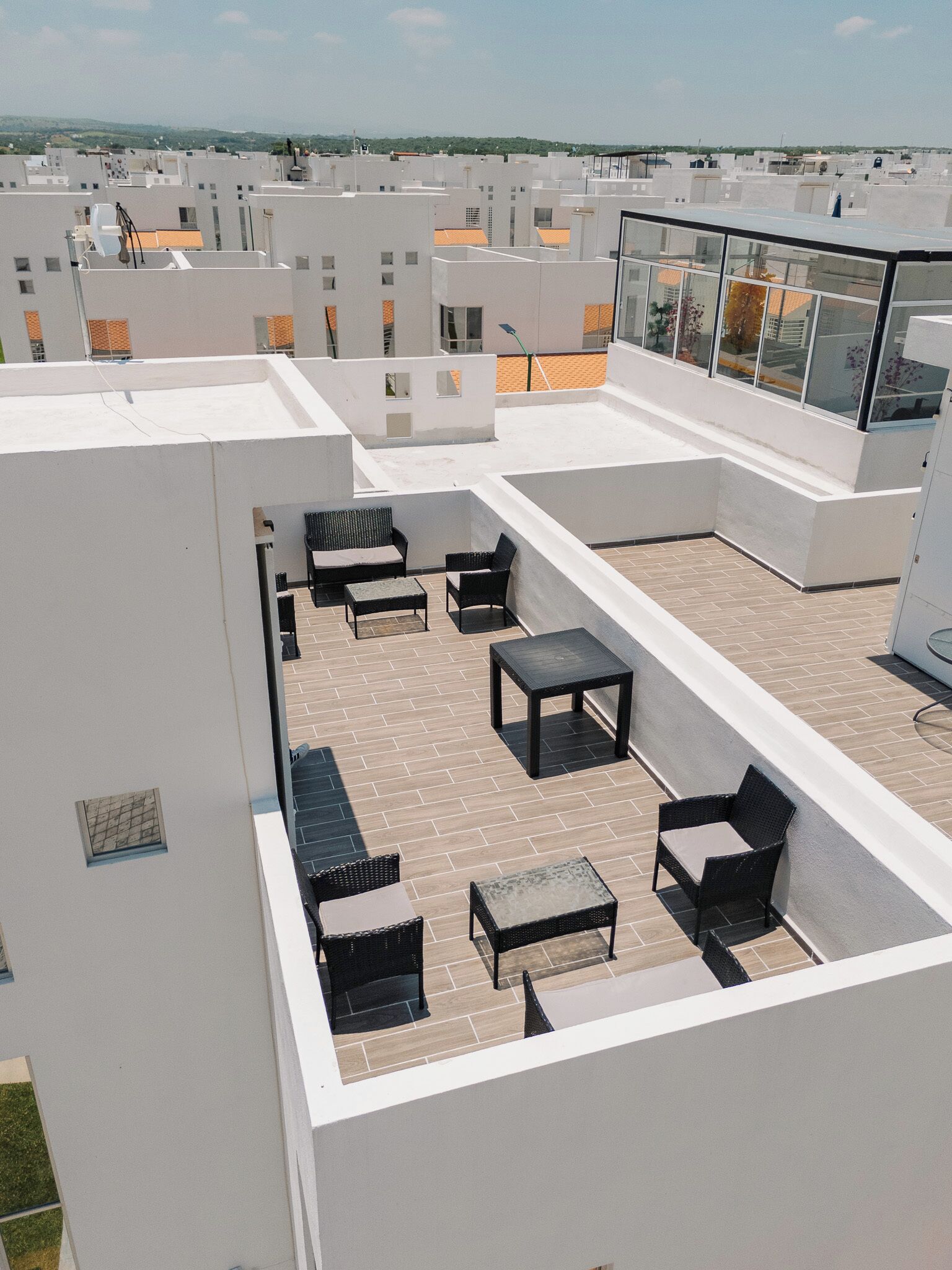 A rooftop terrace with outdoor furniture, a glass balustrade, and a view of surrounding buildings.
