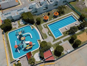 Vista aérea de un complejo de piscinas con una piscina grande, una más pequeña y un tobogán acuático.
