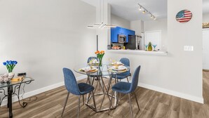 Un comedor moderno con una mesa de vidrio, sillas azules y una cocina al fondo.