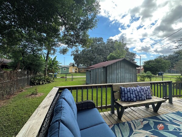 A wooden deck with a blue sofa and a bench, a small shed, and a grassy yard with trees and a fence. - Cottage Downtown Foley/1 mi to Sports Complex/4 mi to OWA/11 mi to beach (Foley)
