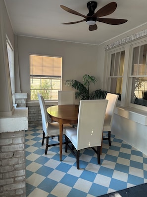 Un coin repas avec une table ronde, quatre chaises, un ventilateur de plafond et un sol à carreaux.